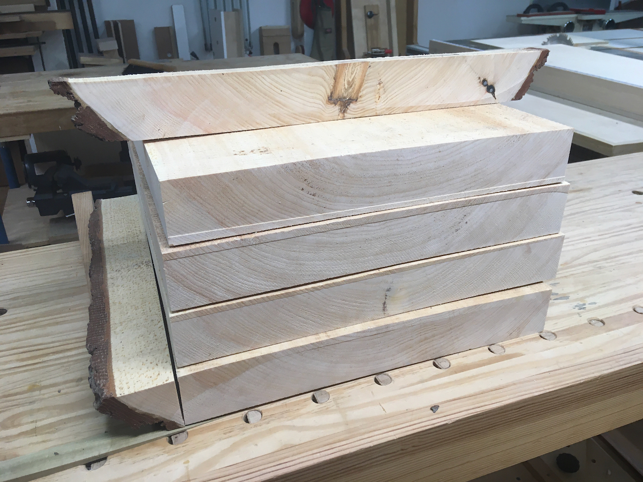 Four rough chair blanks stacked, with a removed edge alongside and a full width cutoff strip on top
